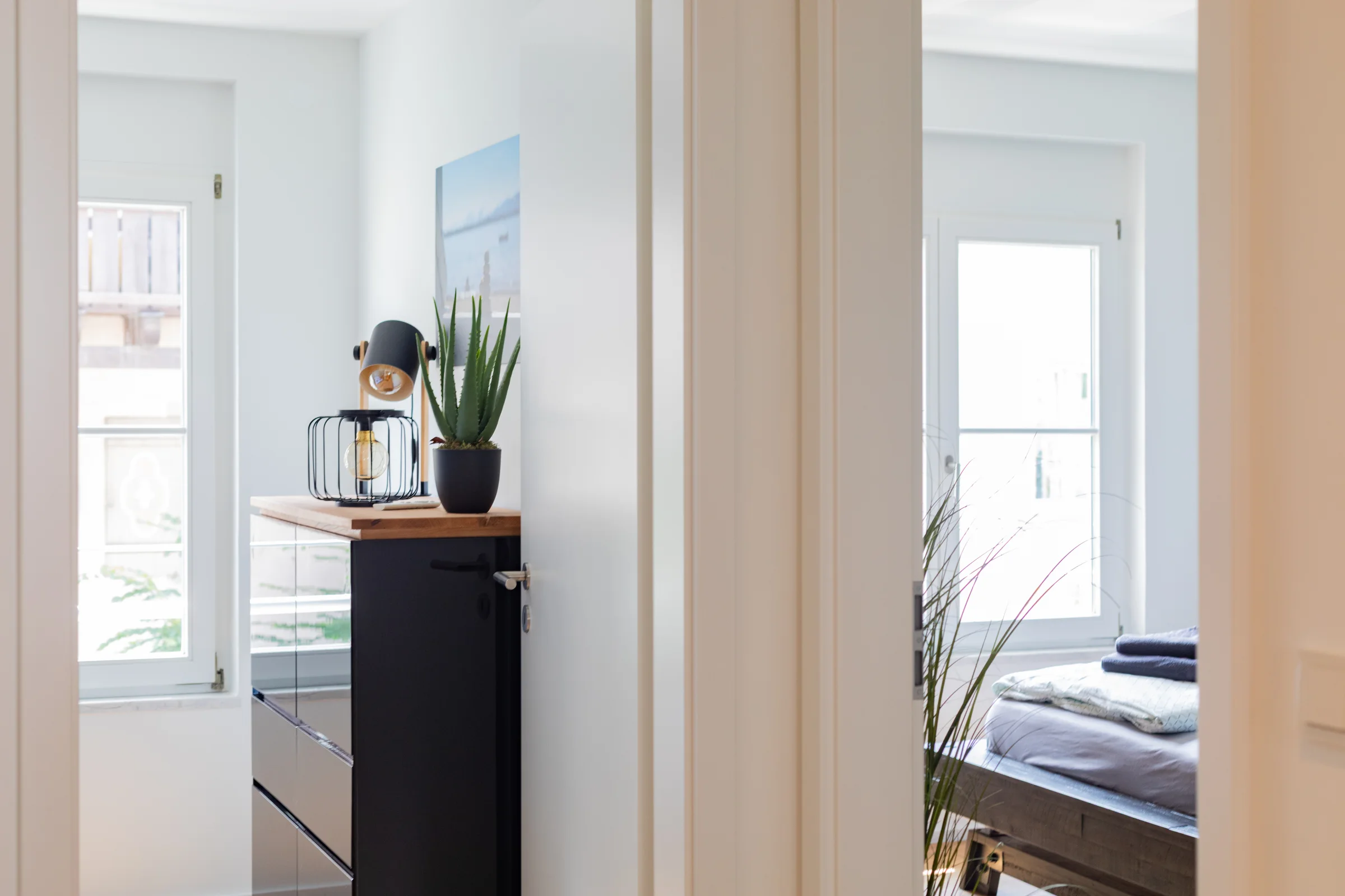 Heller Flur mit schwarzer Kommode, Tischlampe und Topf-Sukkulente, offenes Türblatt und Fensterlicht