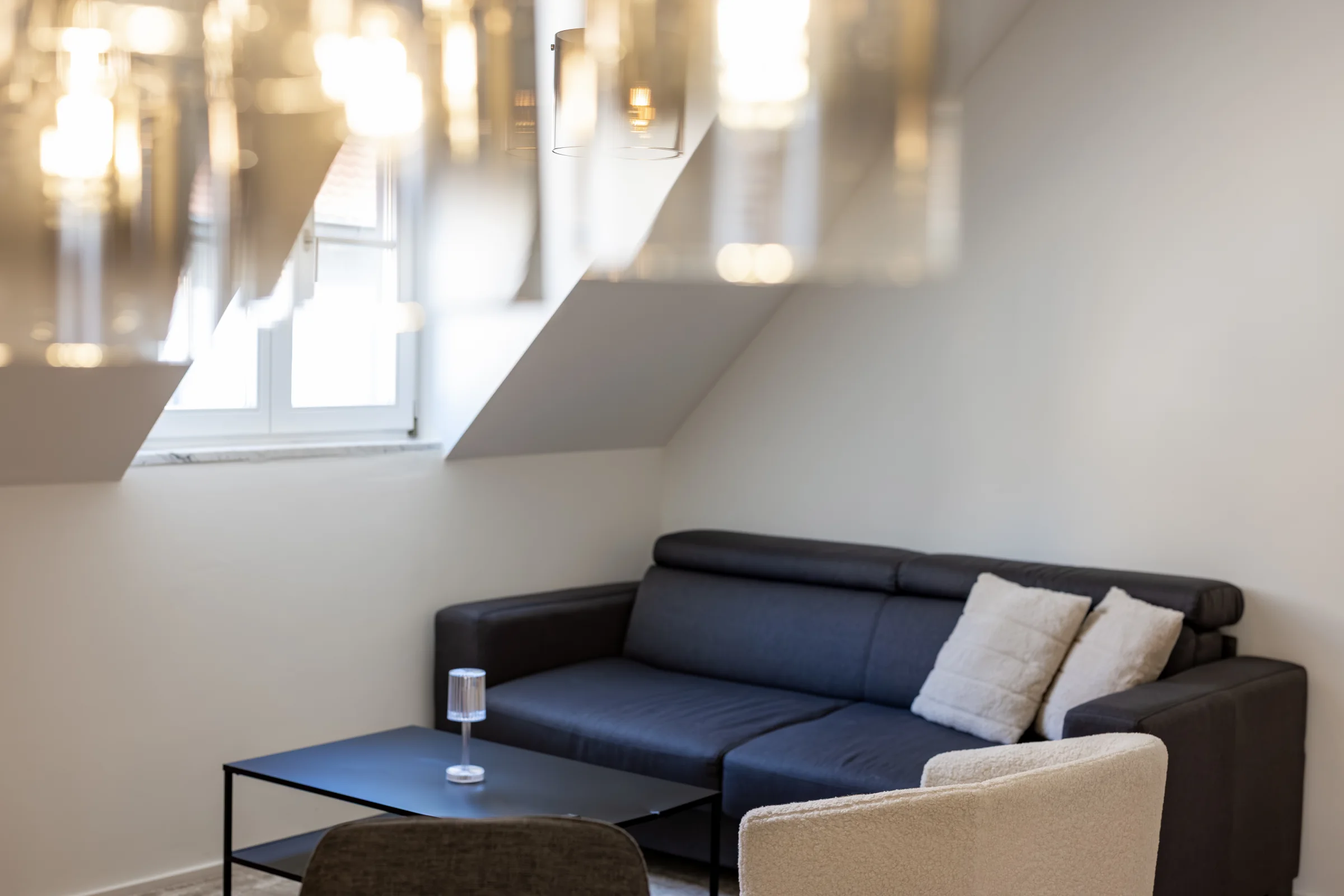Dunkelgraues Sofa mit Kissen, Couchtisch und Fenster in Dachschräge; diffuse Lichtreflexe im oberen Bildbereich