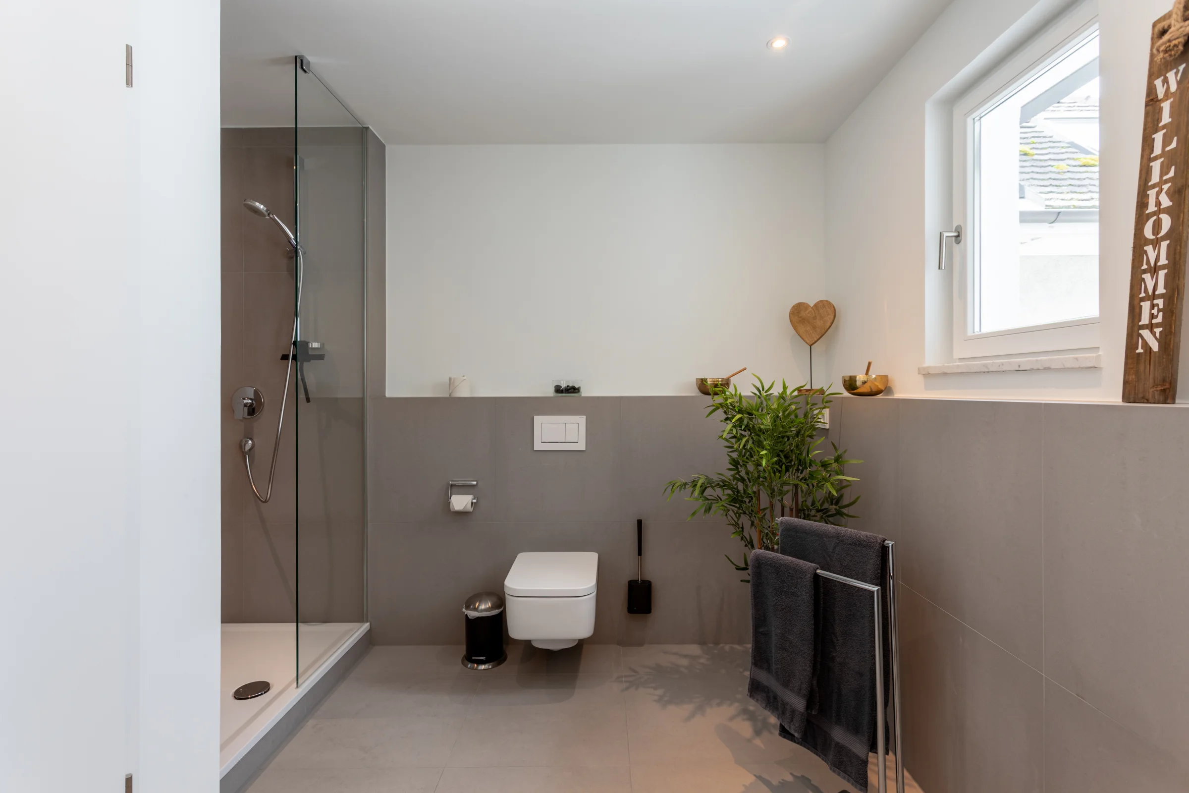 Helles, modernes Badezimmer mit Glasdusche, wandhängendem WC, Fenster, Pflanze und Holzdeko